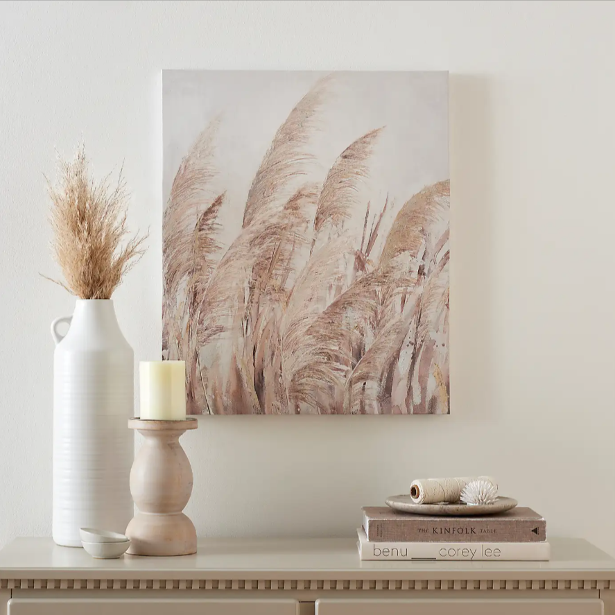 A painting hanging above a dresser holding a vase, candle and stack of books