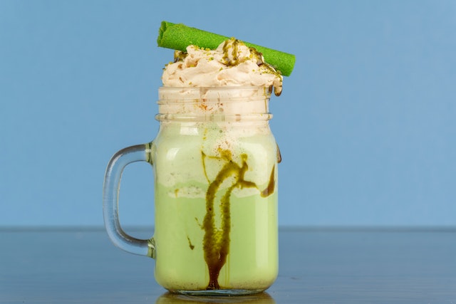 Close-up shot of homemade peppermint green-coloured shake with a green swirl on top with a blue shade background