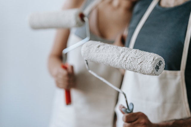 A pair of painters wearing aprons and holding paint rollers soaked in trading paint