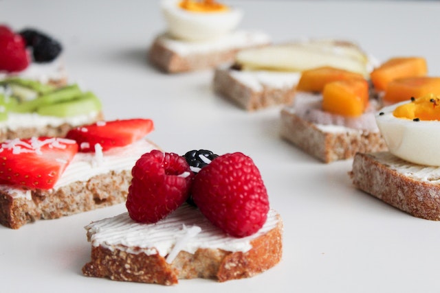 Eight slices of toast covered in cream cheese, assorted fruits and eggs