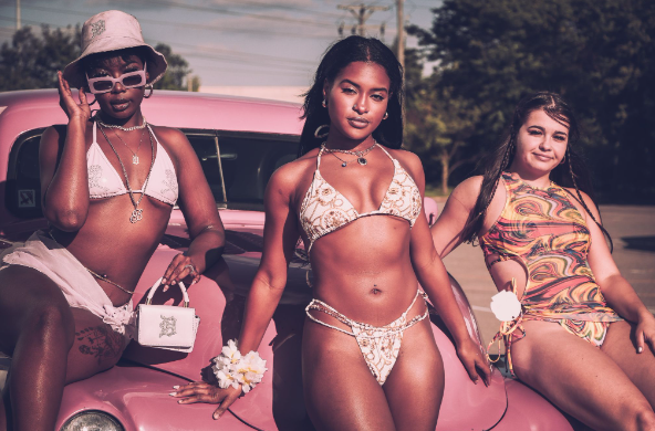 Three women sitting on top of the car who have accessorised their swimming costumes and bikinis