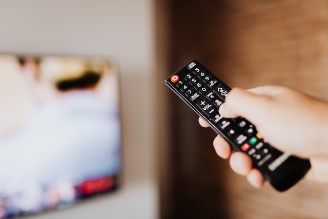 View of a hand holding a remote control with an LG 55 inch TV in the background