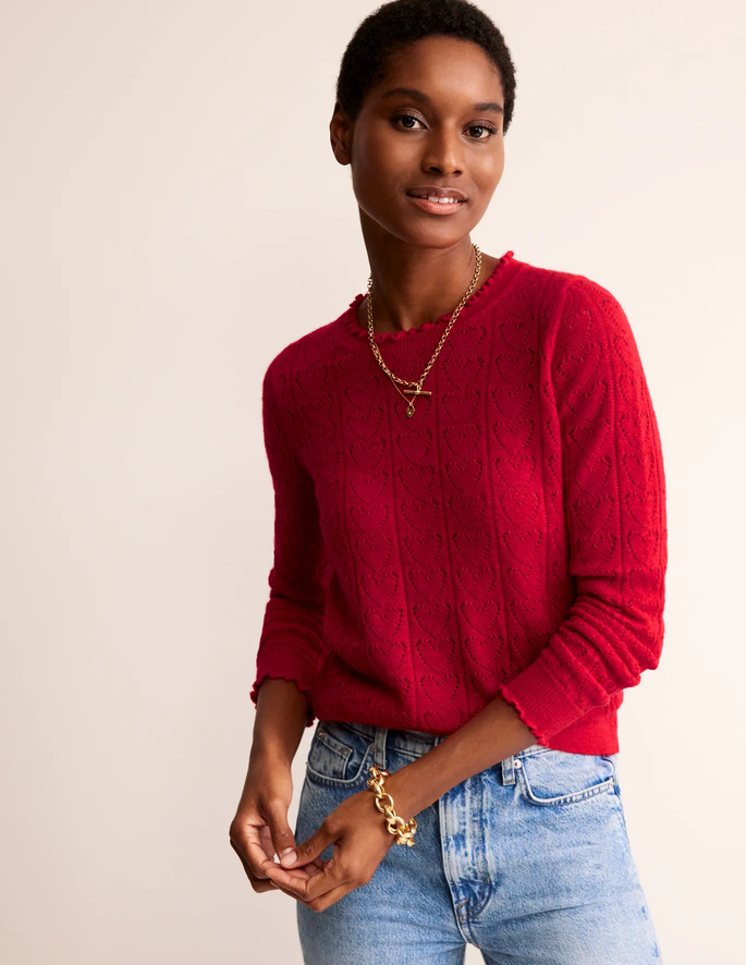 A model posing in a red sweater, a pair of blue jeans and gold jewellery