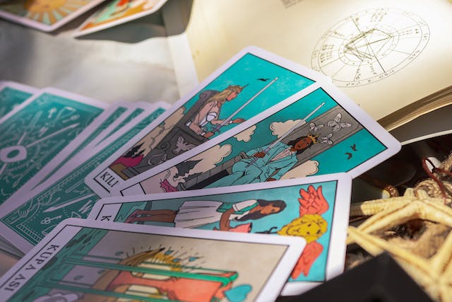 Image: A deck of tarot cards spread out across a table next to a book and sea shells A deck of tarot cards spread out across a table next to a book and sea shells