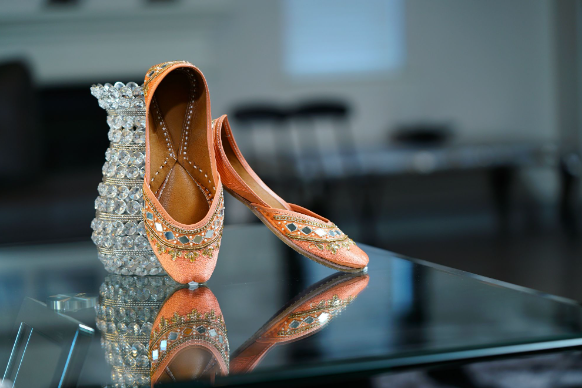 Flat wedding shoes placed on a glass table with a jewelled vase
