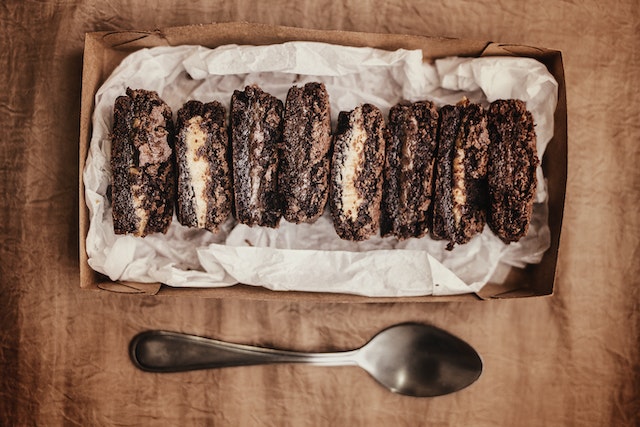 Fudge and mint-flavoured chocolate brownies displayed in a lined rectangular box, with a silver spoon at the bottom