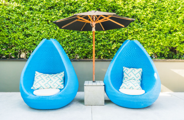 Rattan garden furniture sets: Two blue rattan chairs set outside under an umbrella.