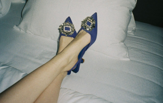 A woman wearing a pair of blue Dorothy Perkins heels on a bed.