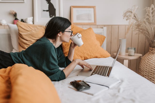 A woman lying on a bed with a laptop looking for the best destinations to travel solo online