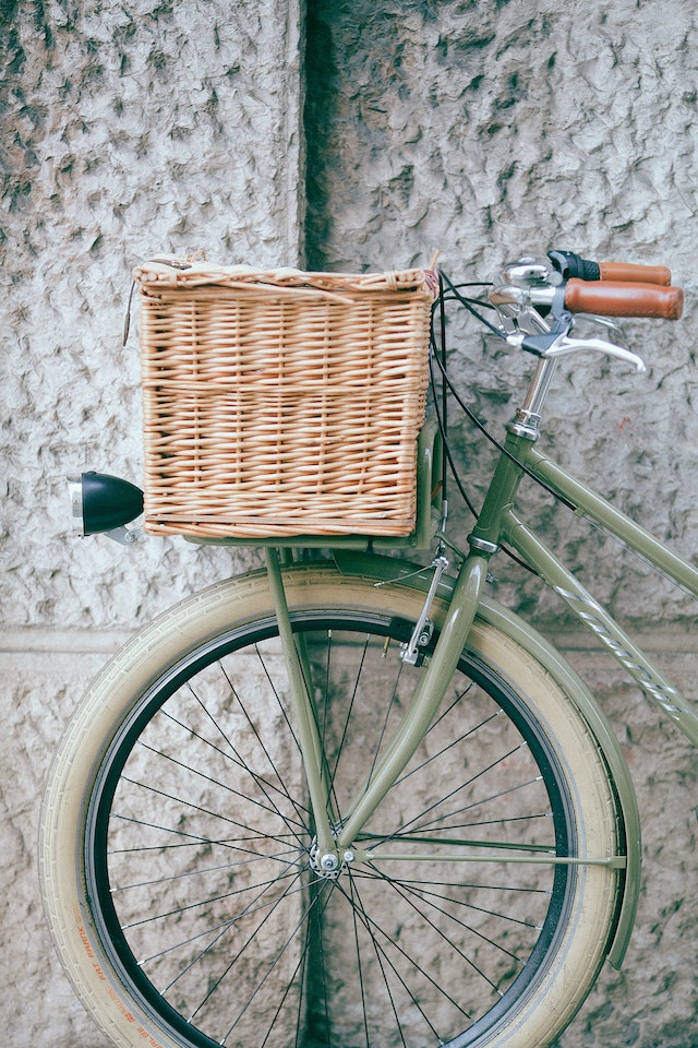 A sage green bicycle with a wicker basket leaning against a course brick wall