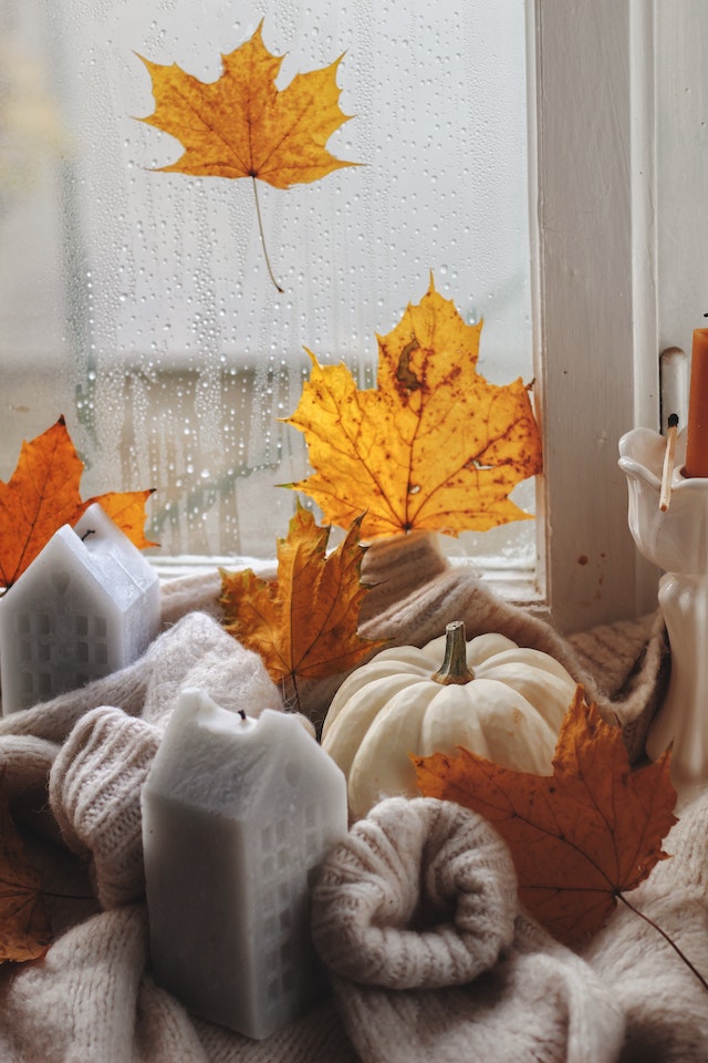 Pumpkin ornaments UK: A pumpkin, leaves and candles bundled up in a sweater on a windowsill