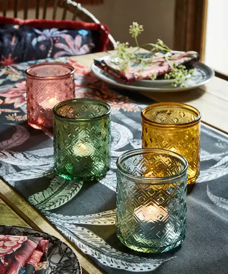 Four glass tealight holders standing on top of a table runner on a set dining table