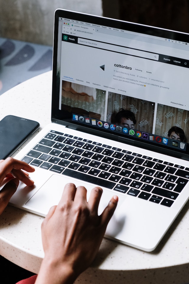 A close-up image of a person scrolling on a laptop with their phone alongside them