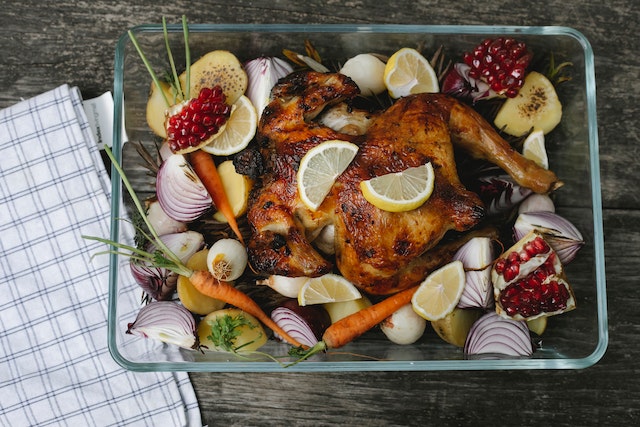A baking dish filled with chopped vegetables, fruits and a whole roast chicken