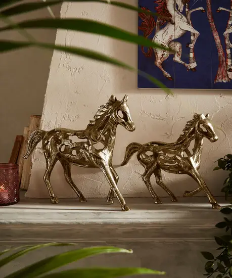 A pair of gold cast iron horse statues standing on a table in front of a beige wall