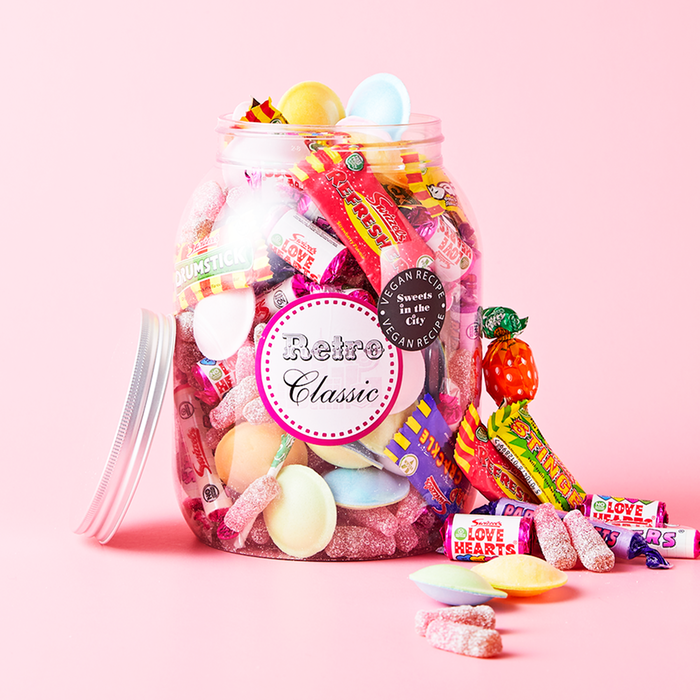 A glass jar of vintage sweets standing on a pink background with the lid leaning against it