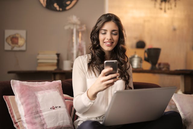 Image: A woman holding her phone and laptop while signing up for an Amazon Prime membership A woman holding her phone and laptop while signing up for an Amazon Prime membership