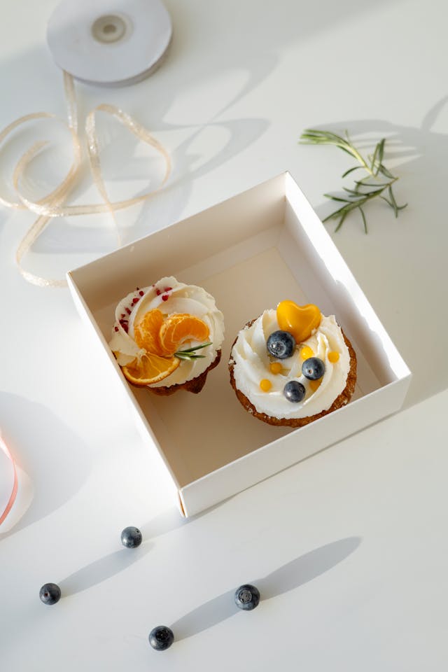 Two mimosa cupcakes topped with orange slices standing in a white box on a countertop