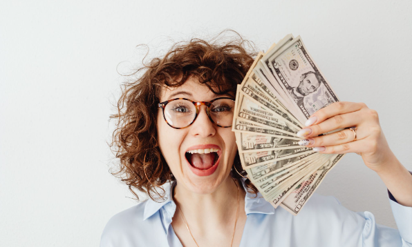 A woman smiling & holding the money she saved on her drive-in cinema visit