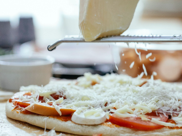 Mozzarella cheese being grated on pizza : Italian pizza vs American pizza