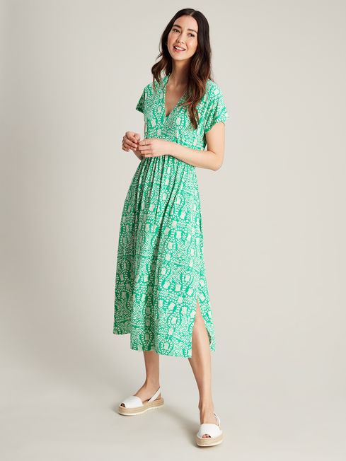A model posing in a green beach dress and white sandals on a white background