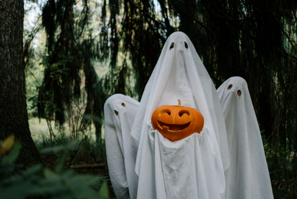 3 people dressed in Halloween scary costumes holding a carved pumpkin