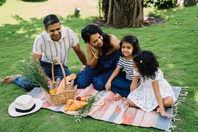 A family of four having a picnic for Mother’s Day on the grass with a picnic basket and blanket