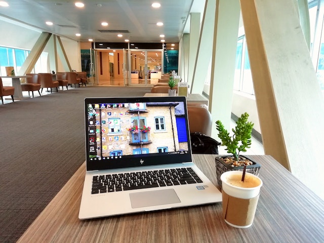 A cup of coffee and pot plant next to a silver HP touch screen laptop on a wooden table