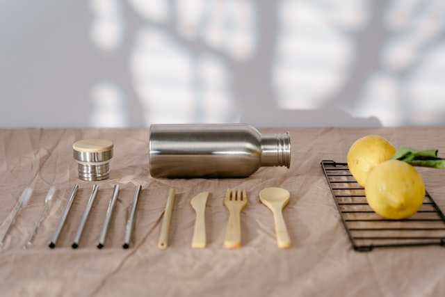 A set of metal straws, wooden cutlery, a water bottle and a pair of lemons on a counter