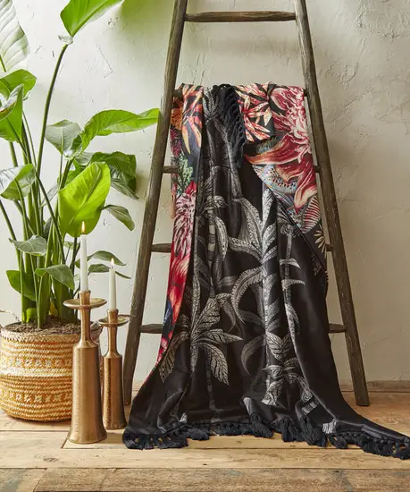 A black, white and pink floral throw draped over a decorative ladder next to some candles