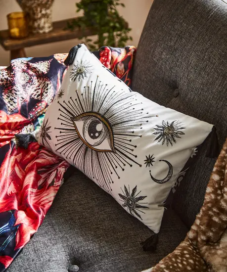 A cushion with an eye design laying on top of a throw blanket on an armchair