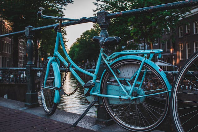 A blue road bicycle that is chained to a fence along a river