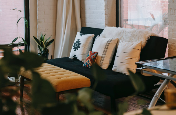 Image: A 2-seater sofa bed with white cushions and a throw blanket inside a studio apartment. A 2-seater sofa bed with white cushions and a throw blanket inside a studio apartment.