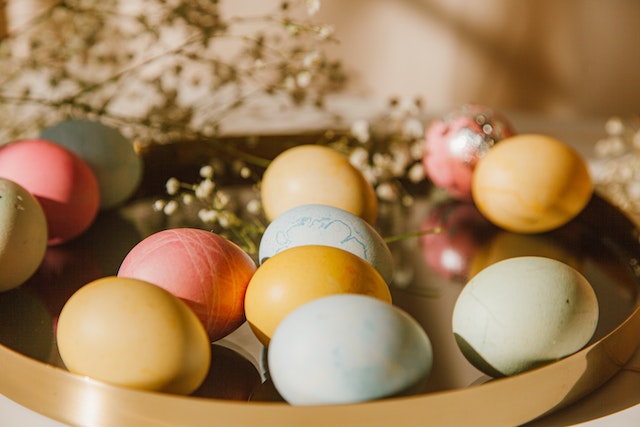 A tray holding a dozen colourful chocolate Easter eggs surrounded by some flowers