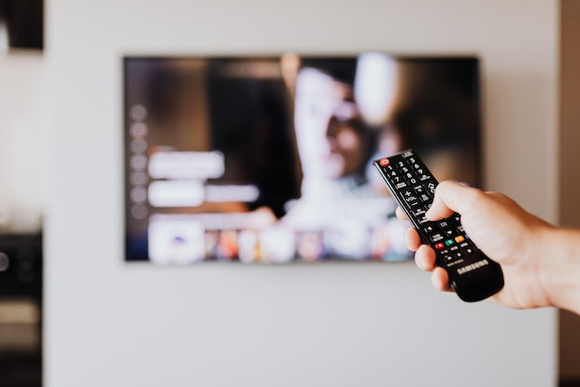 View of someone holding a remote control with the best 55 inch TV UK in the background