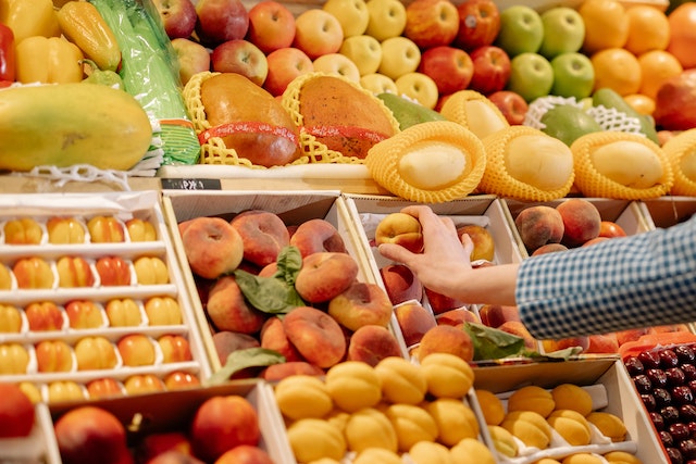 shopping habits in the UK: A person picking up a peach from a fruit display