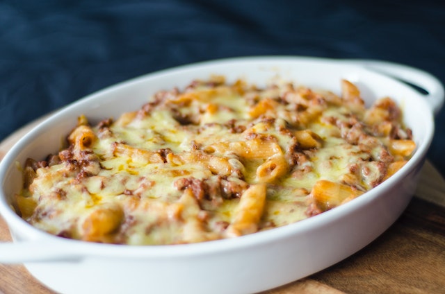 Creamy delicious mac and cheese pasta casserole in a white oven dish, all set on a wooden table