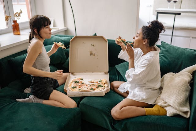Image: ideas for Valentine's Day: Two women eating pizza out of the box on the couch ideas for Valentine's Day: Two women eating pizza out of the box on the couch