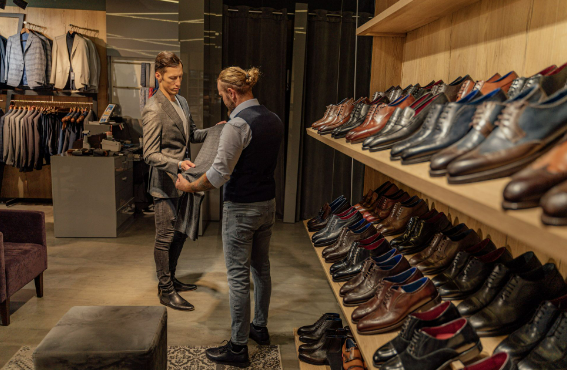 Two men shopping for suits and shoes in a men’s clothing store.