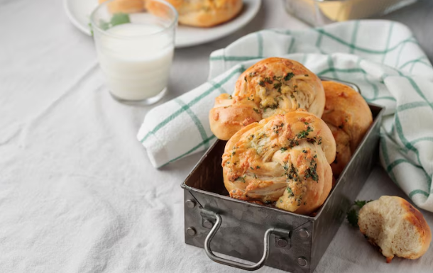 Prosecco cocktails with vodka: Garlic bread knots in a bread tin and tea towel next to it with a glass of milk on the top left