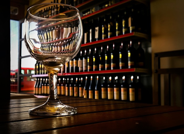 Majestic Wine in the UK: Empty wine glass on a wooden table with shelves filled with different bottles of wine in the background.