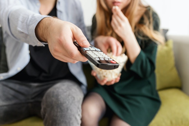 A man holding a remote control next to a woman with popcorn getting ready to watch Love Island