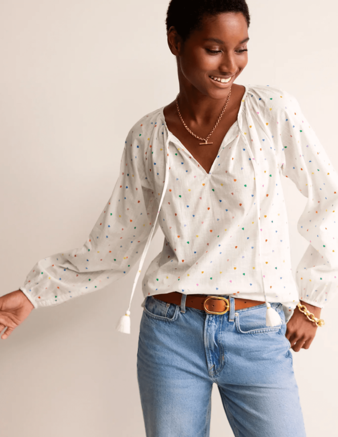 A model posing in a Serena cotton blouse and blue jeans in front of a beige background