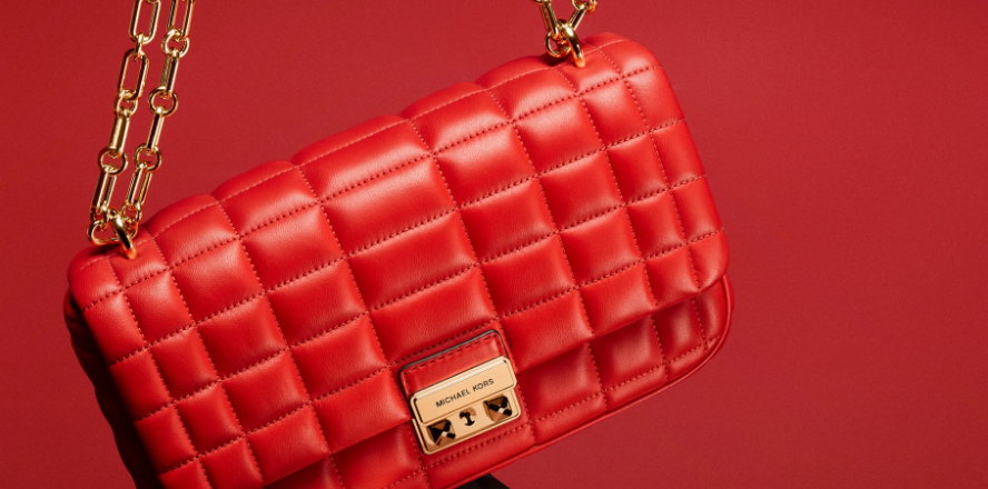 Red bold statement Michael Kors shoulder bag with gold chain sling on a maroon background.