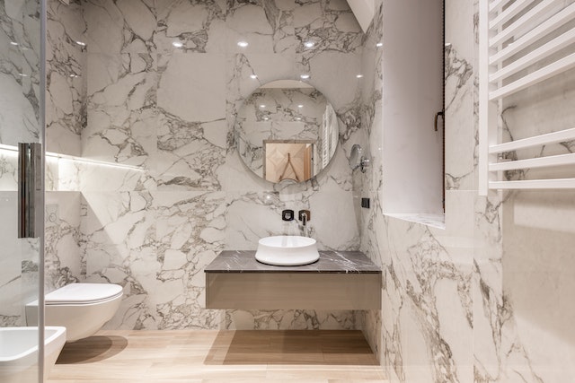 A marble bathroom with a vanity, mirror, toilet, urinal and glass partition