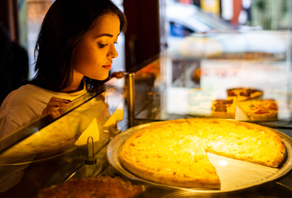 Woman ordering an american pizza slice from the pizza display
