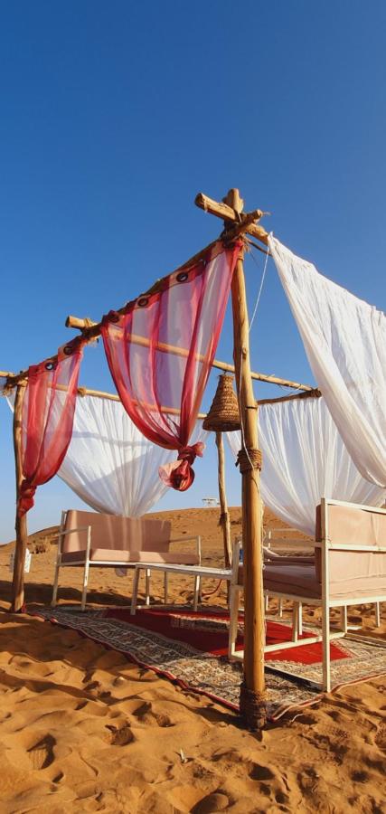 Image: An outdoor seating area made from wooden logs and cloth standing on dessert sand An outdoor seating area made from wooden logs and cloth standing on dessert sand