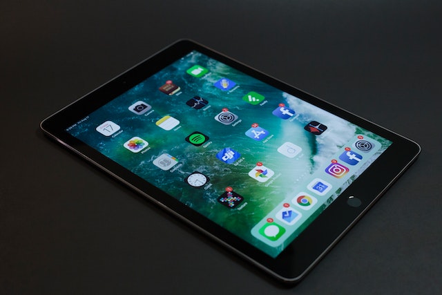 A black refurbished iPad that is turned on and shows the app home screen