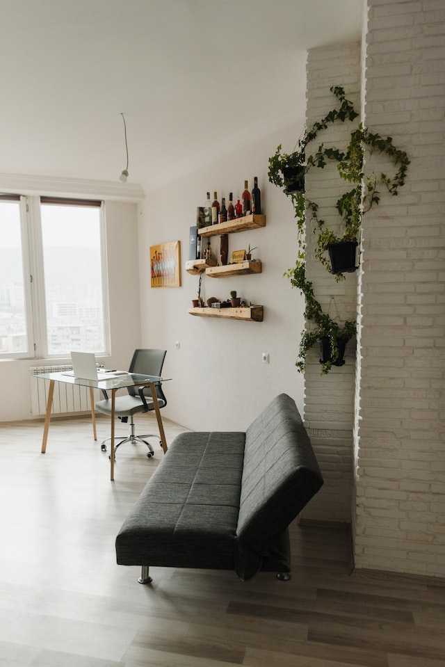 A grey cheap sofa bed standing in front of a brick wall covered in vines