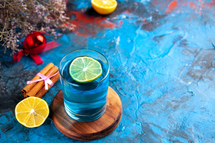 Prosecco cocktails with vodka: Blue lagoon cocktail with a lemon slice in it placed on a wooden coaster with cinnamon sticks wrapped on the side.